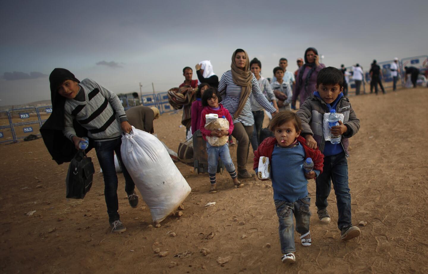 File photo of Kurdish Syrian refugees carrying their belongings after crossing the Turkish-Syrian border near the southeastern town of Suruc in Sanliurfa province